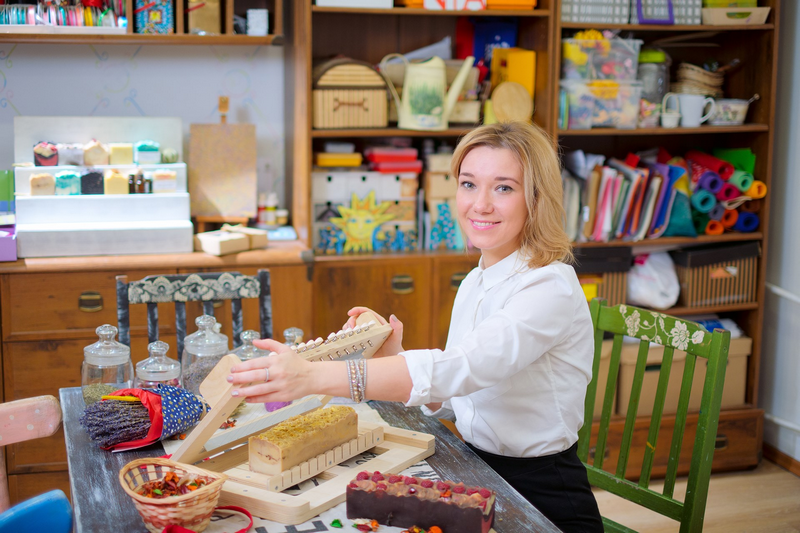 A woman creating handmade soap at a craft table filled with various natural ingredients and tools.